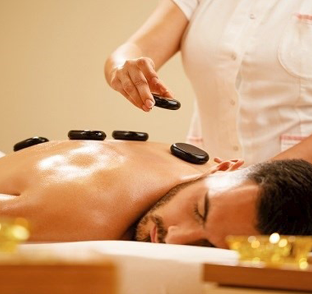 A man is practicing self-care by receiving a hot stone massage, which helps relieve muscle tension and promote deep relaxation