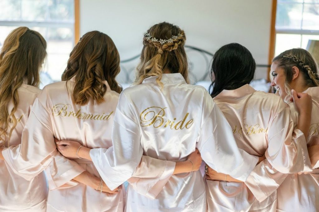 Bride and bridesmaids in silk robes embracing during a relaxing spa day for wedding party