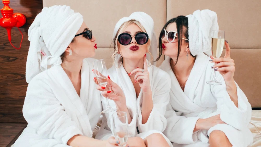 Bridesmaids in white robes celebrating with champagne during a spa day for wedding party